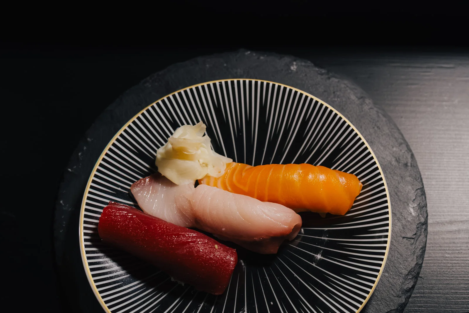 Nigiri von Thunfisch, Lachs und Gelbschwanz auf einem schwarzen Teller